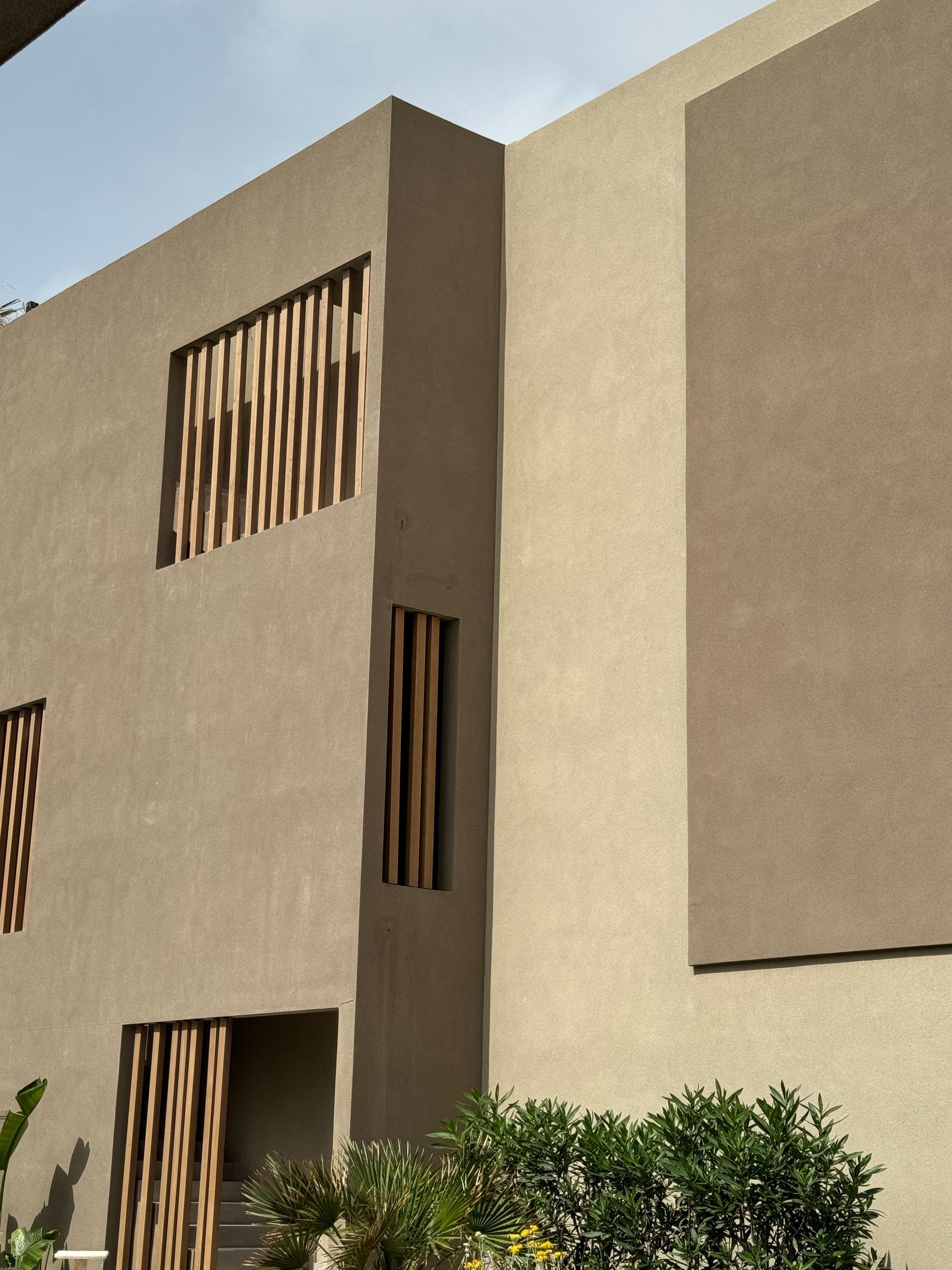 Exterior del edificio de color canela con listones de madera en las ventanas y arbustos en la parte inferior.