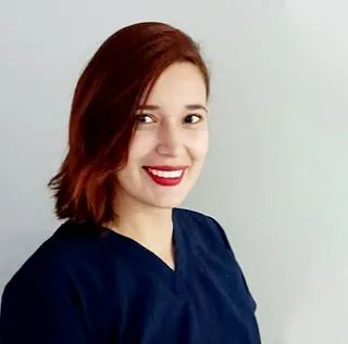 Una mujer con cabello rojo viste un uniforme azul y sonríe.