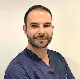 Un hombre con barba viste un uniforme azul y sonríe a la cámara.