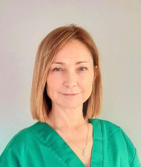 Una mujer que lleva una blusa verde y un collar sonríe para la cámara.