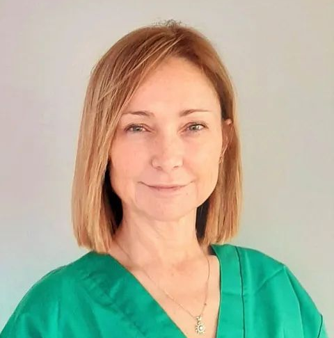 Una mujer que lleva una blusa verde y un collar sonríe para la cámara.