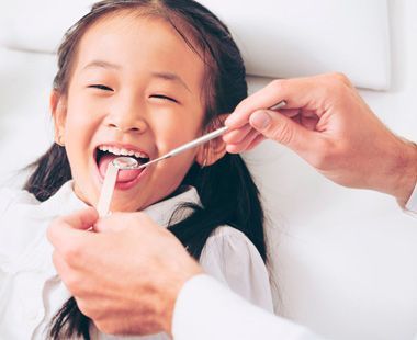 A una niña le están examinando los dientes un dentista.