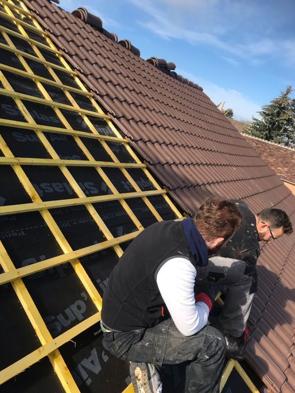 Deux ouvriers installent des liteaux jaunes sur un toit de tuiles.