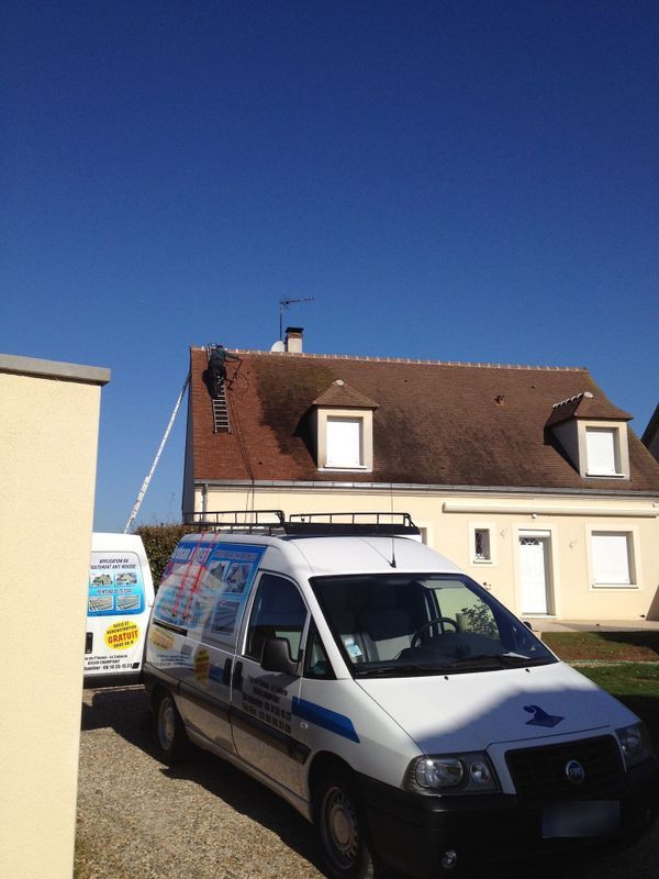 Une camionnette blanche garée dans une rue résidentielle ensoleillée, à côté d'une maison couleur crème au toit rouge.