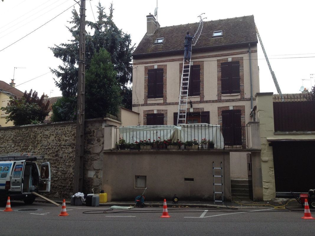 Maison de trois étages derrière une barrière, avec des cônes et un véhicule stationné dans la rue.