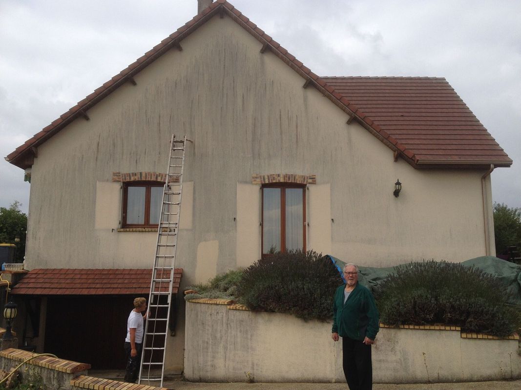 Extérieur d'une maison beige avec une échelle et deux personnes devant une maison.