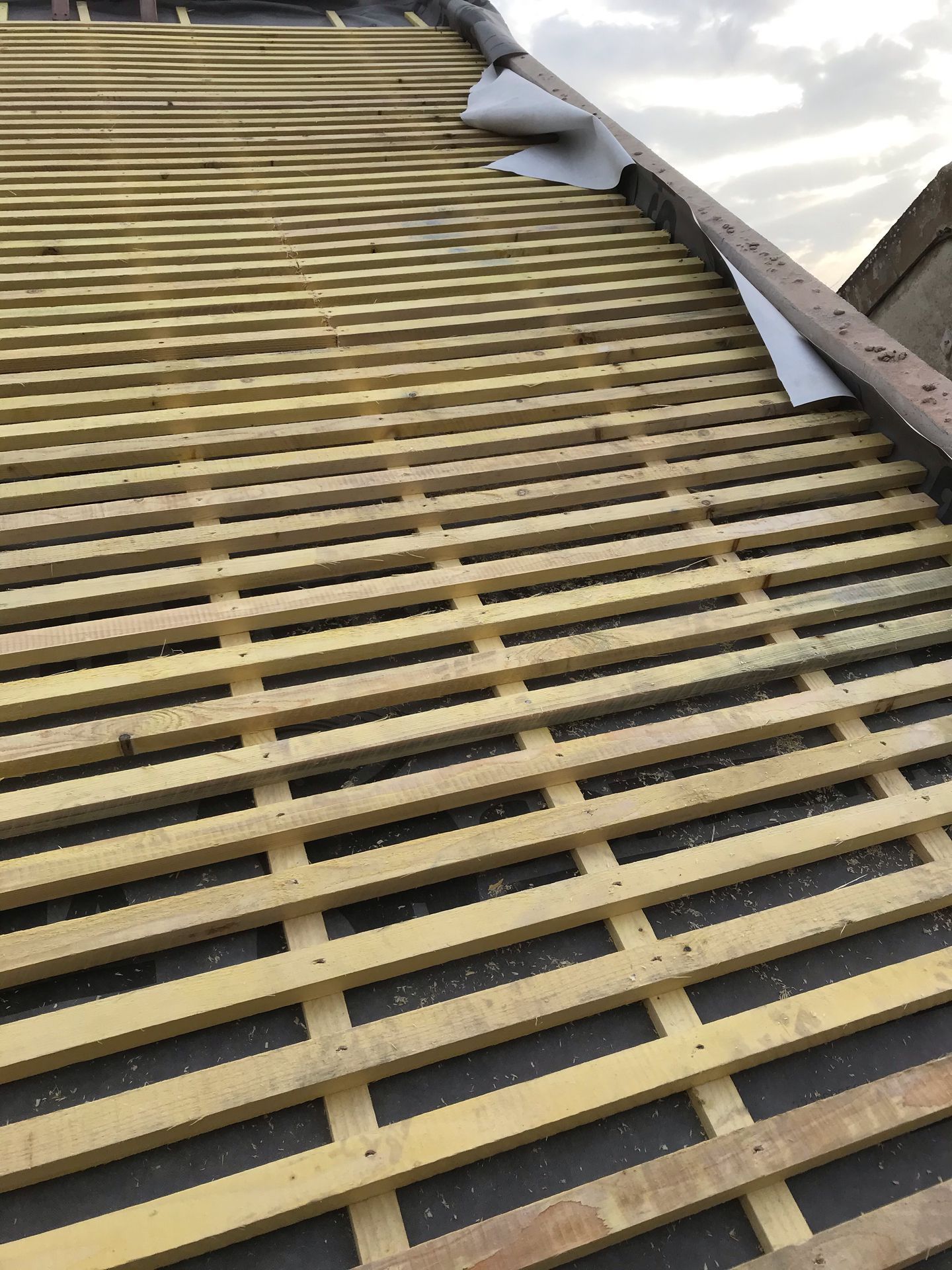 Toiture partiellement dénudée avec liteaux de bois apparents et une tôle de couverture enroulée en bordure.