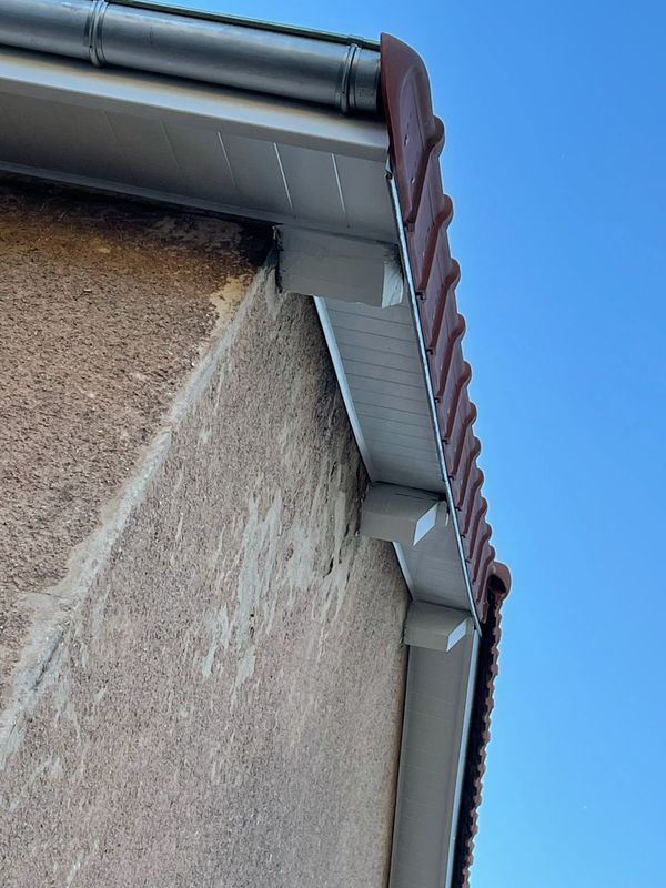 Angle extérieur d'une maison avec gouttière et descente pluviale blanches.
