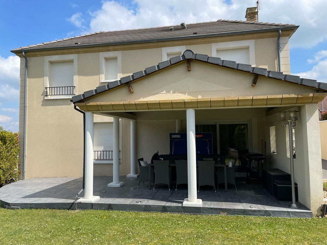 Maison à deux étages avec patio couvert et colonnes blanches sur une pelouse.