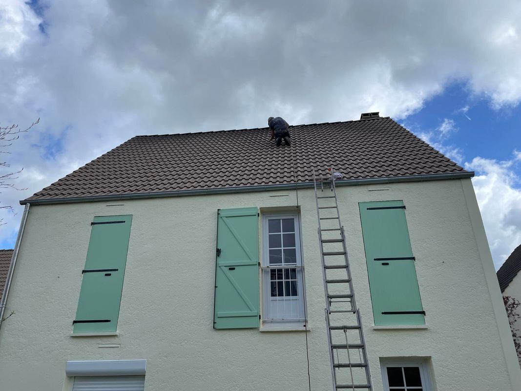 Maison aux volets vert menthe et une échelle sur le toit.