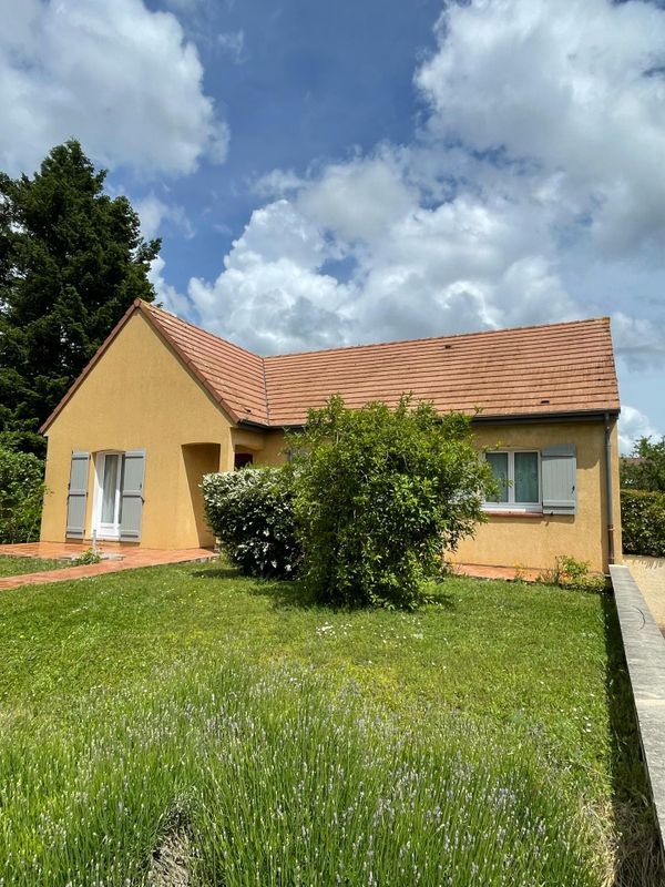 Maison jaune au toit de tuiles, pelouse verte et ciel nuageux.