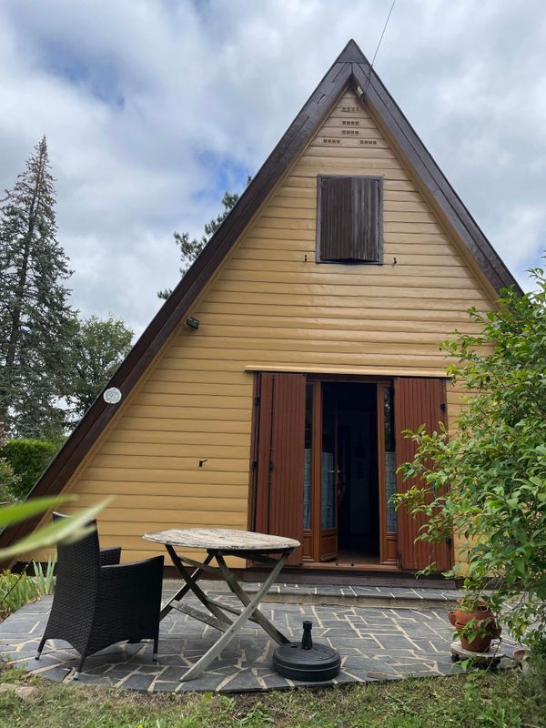 Une petite cabane en bois en forme de A, avec une porte ouverte, une table de patio et des chaises.