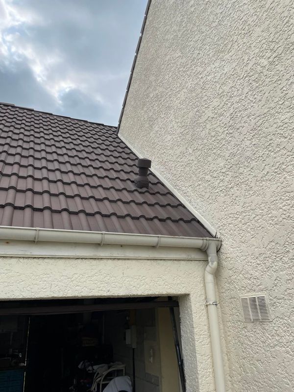 Vue extérieure d'une maison avec un toit en bardeaux bruns, des murs blancs et une entrée de garage sombre.