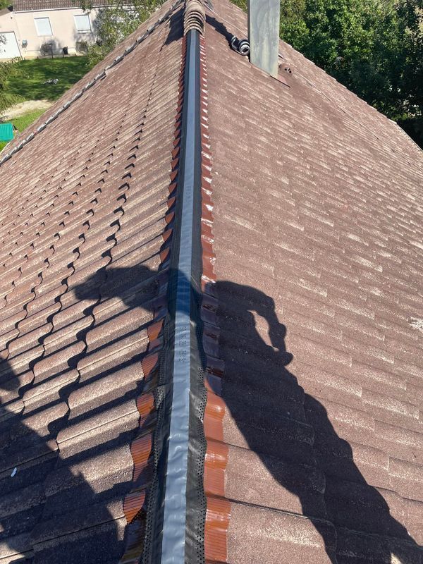 Faîtage recouvert de bardeaux bruns et muni d'une grille de ventilation métallique.