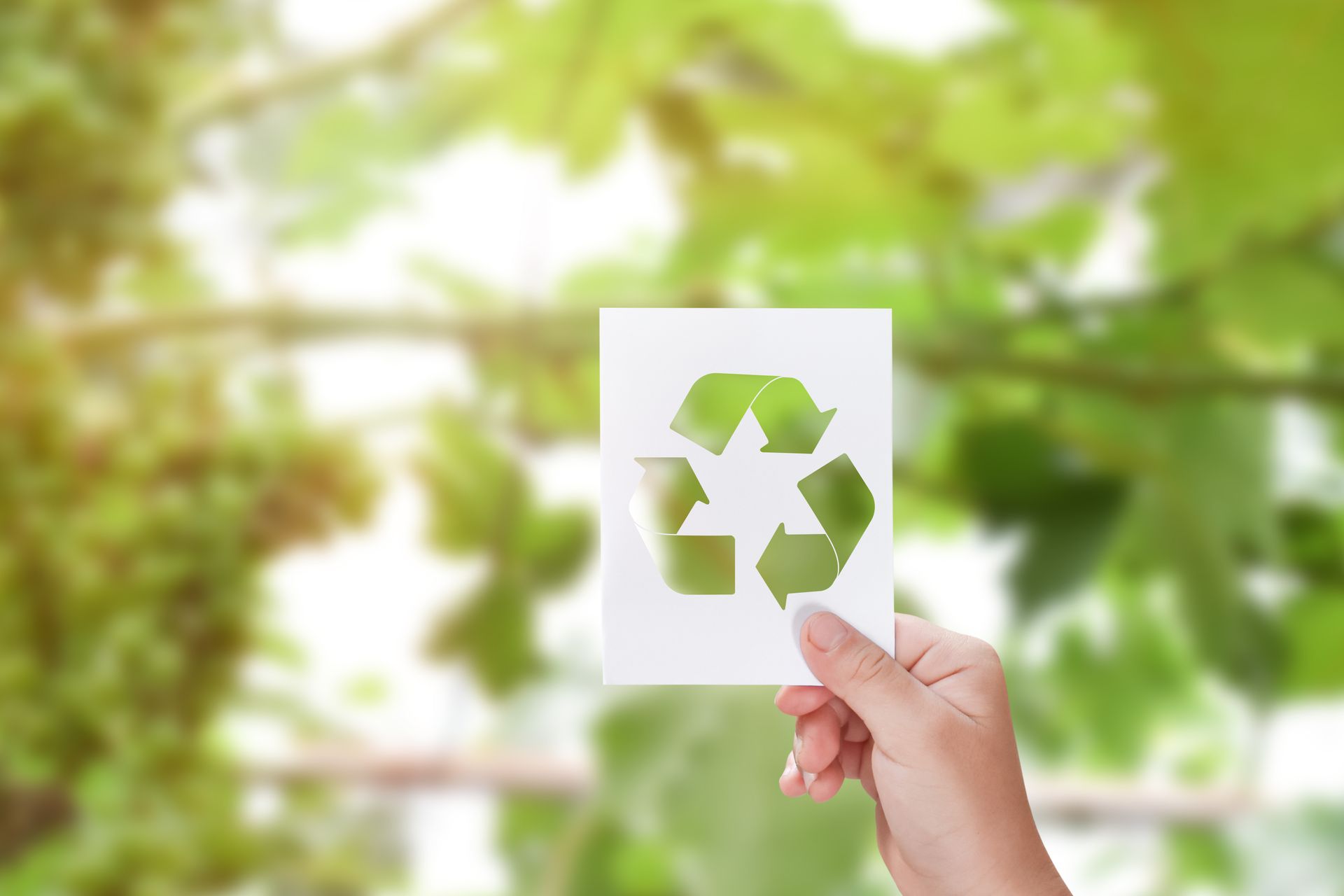 Main tenant une feuille de papier blanc sur laquelle est découpé le symbole du recyclage.