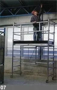 Une personne sur un échafaudage mobile atteignant le plafond d'un entrepôt.