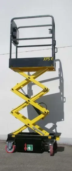 Un élévateur à ciseaux jaune avec une base noire et un garde-corps sur une surface grise.