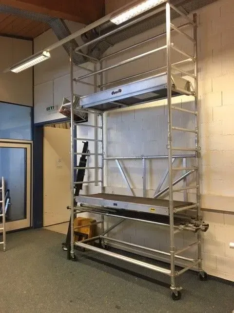 Échafaudage roulant en aluminium à l'intérieur d'un bâtiment, près d'une porte.