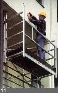 Un homme portant un casque jaune travaille sur un bâtiment depuis une plate-forme d'échafaudage.
