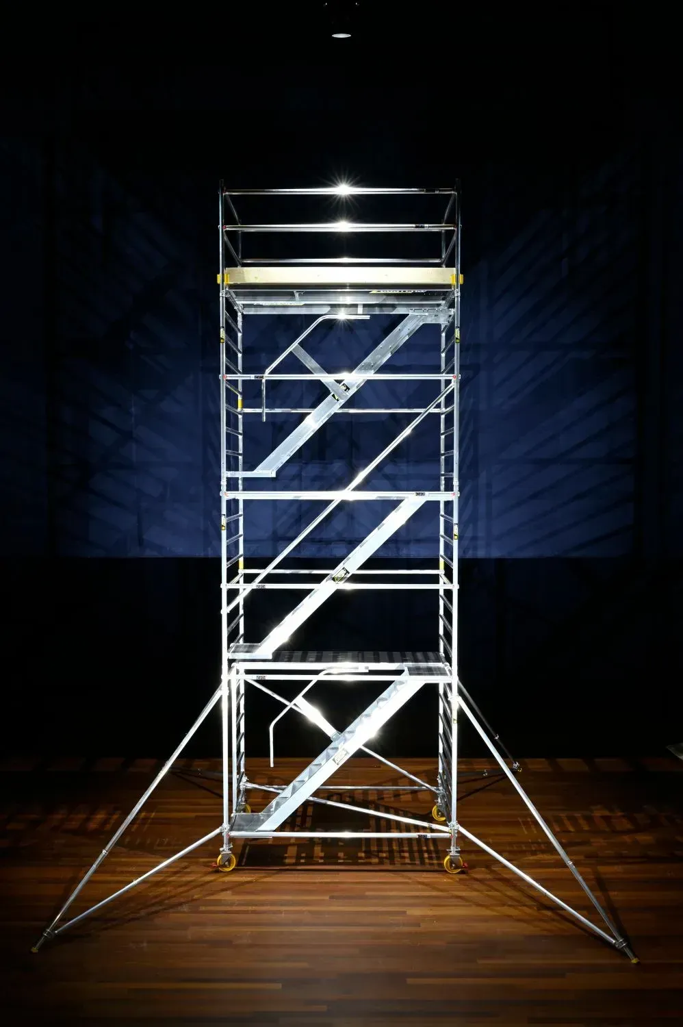 Structure d'échafaudage argentée dans un espace de galerie sombre, éclairée par des lumières vives sur son sommet