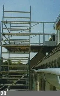 Échafaudage sur le côté d'un bâtiment, atteignant la ligne de toit. Structure métallique, ciel lumineux.