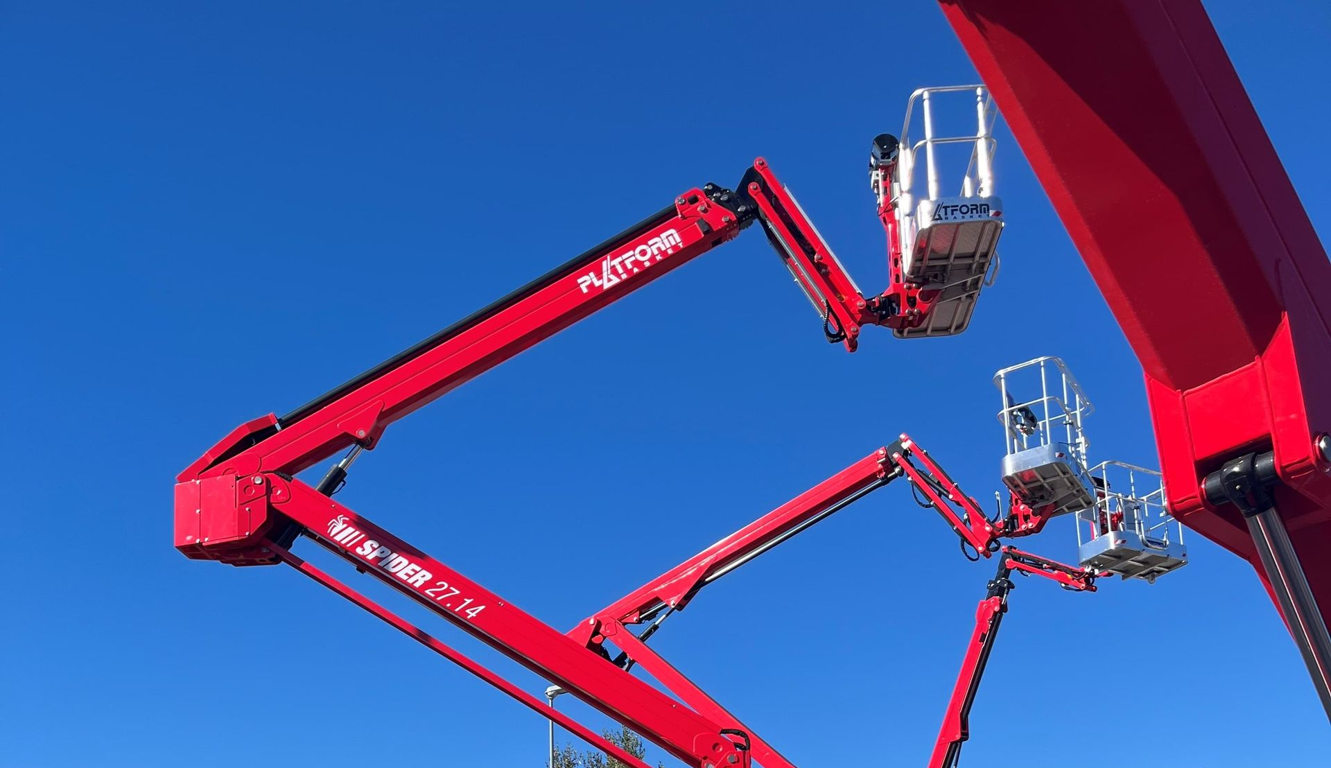 Nacelles élévatrices rouges à plateformes surélevées se détachant sur un ciel bleu clair