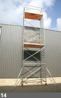 Tour d'échafaudage, en métal argenté, avec deux plates-formes orange contre un mur gris.