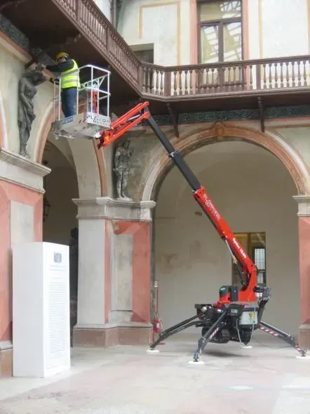 Un ouvrier sur une plate-forme élévatrice répare la façade ornée d'un bâtiment dans une cour intérieure.