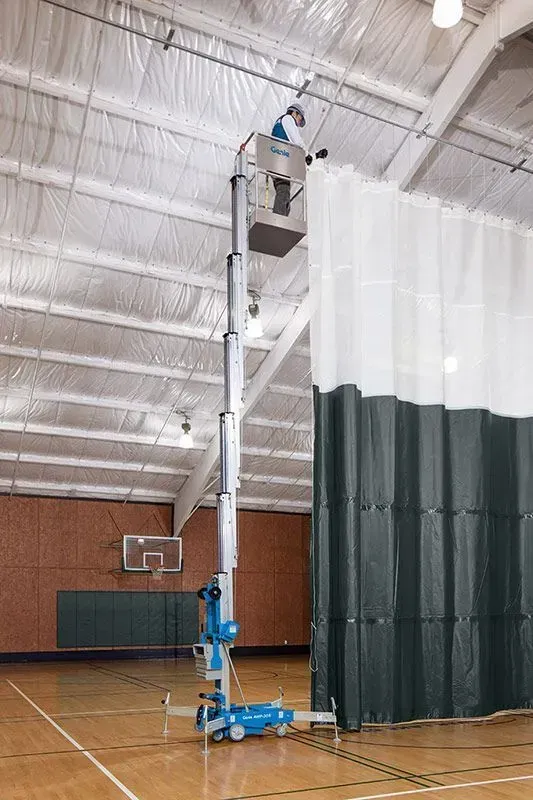 Une personne dans un ascenseur travaille sur le plafond d'un gymnase, à côté d'un rideau.