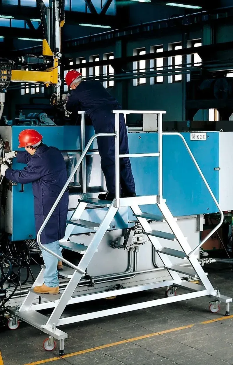 Deux ouvriers sur une plate-forme roulante en aluminium, réparant des équipements industriels dans une usine.