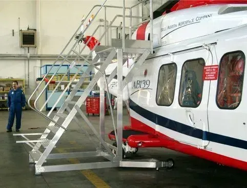 Escalier d'accès en aluminium à côté d'un hélicoptère rouge et blanc dans un hangar ; une personne se tient à proximité.