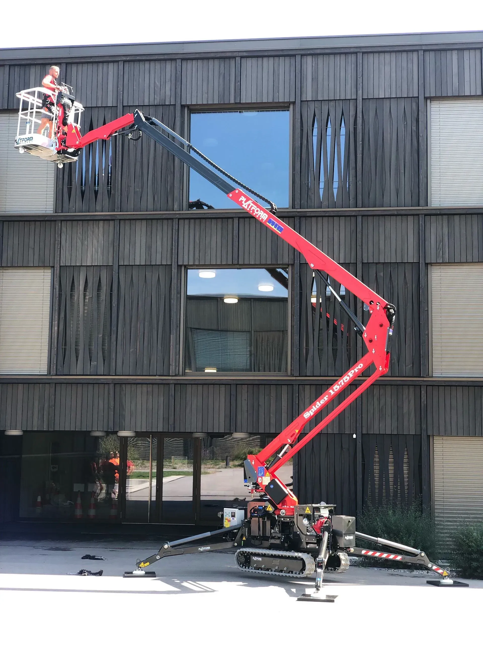 Une nacelle élévatrice rouge avec un ouvrier répare la façade d'un bâtiment. 