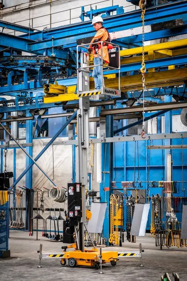 Ouvrier en combinaison orange sur une plate-forme élévatrice mobile dans un environnement industriel