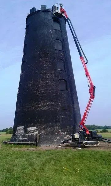Un grand moulin à vent noir sur lequel travaille un ascenseur rouge, installé dans un champ herbeux.