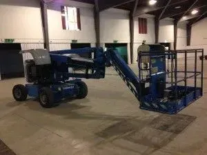 Nacelle élévatrice bleue dans un grand espace intérieur ouvert, probablement un entrepôt ou une salle d'événements.