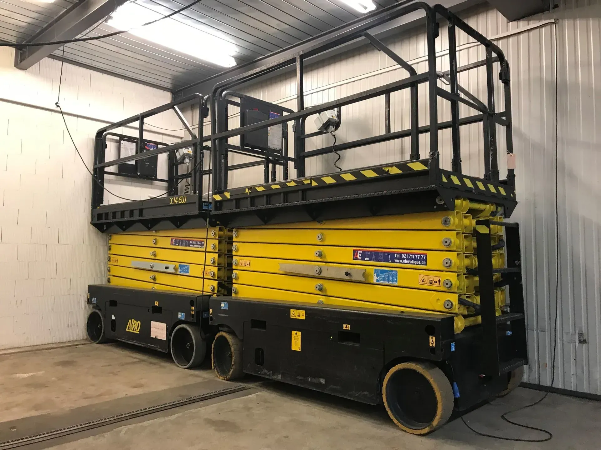 Nacelle élévatrice à ciseaux jaune et noire dans un entrepôt, avec plate-forme surélevée.