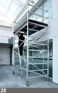 Un homme sur un échafaudage mobile à l'intérieur d'un bâtiment, travaillant sur une plate-forme