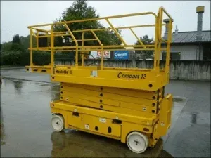 Nacelle élévatrice à ciseaux jaune JLG Compact 12 sur une surface humide à l'extérieur, prête pour un accès vertical.