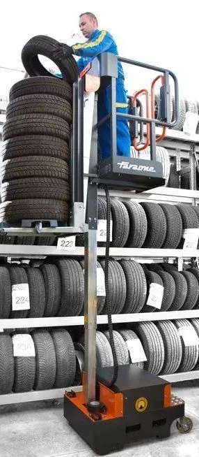 Un mécanicien sur un élévateur place un pneu sur une pile dans un atelier de pneus.