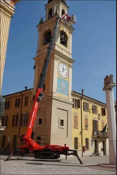 Une grue rouge élève des ouvriers jusqu'au sommet d'une haute tour de l'horloge sur une place de la ville.