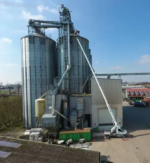 Silos à grains avec un élévateur monté sur camion étendu vers la structure par une journée ensoleillée.