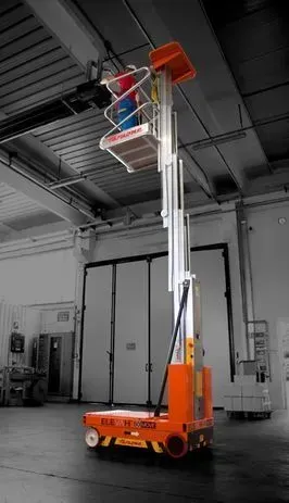 Plateforme de travail aérienne orange et argentée avec une personne à l'intérieur ; dans un entrepôt.