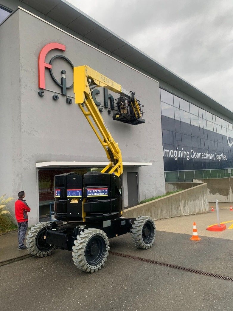 Un ouvrier, à bord d'une nacelle élévatrice, installe une enseigne de magasin à l'extérieur d'un bâtiment.