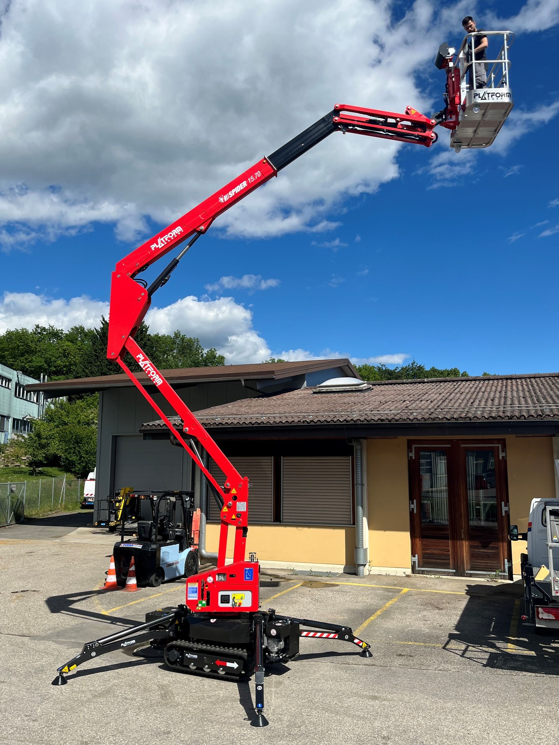 Une nacelle élévatrice rouge avec un ouvrier répare la façade d'un bâtiment. 