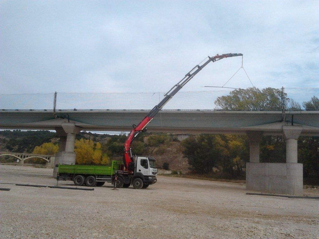 Un camión con una grúa acoplada está estacionado debajo de un puente.