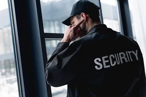 Un guardia de seguridad está mirando por una ventana y hablando por un teléfono celular.