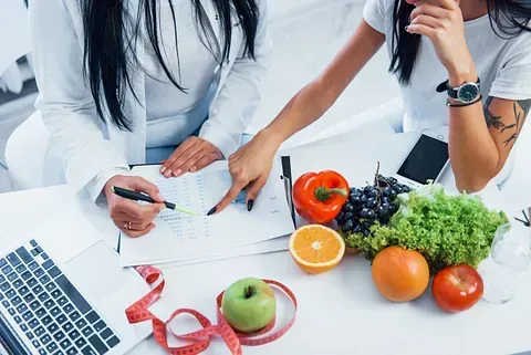 Dos mujeres están sentadas en una mesa con frutas y verduras.
