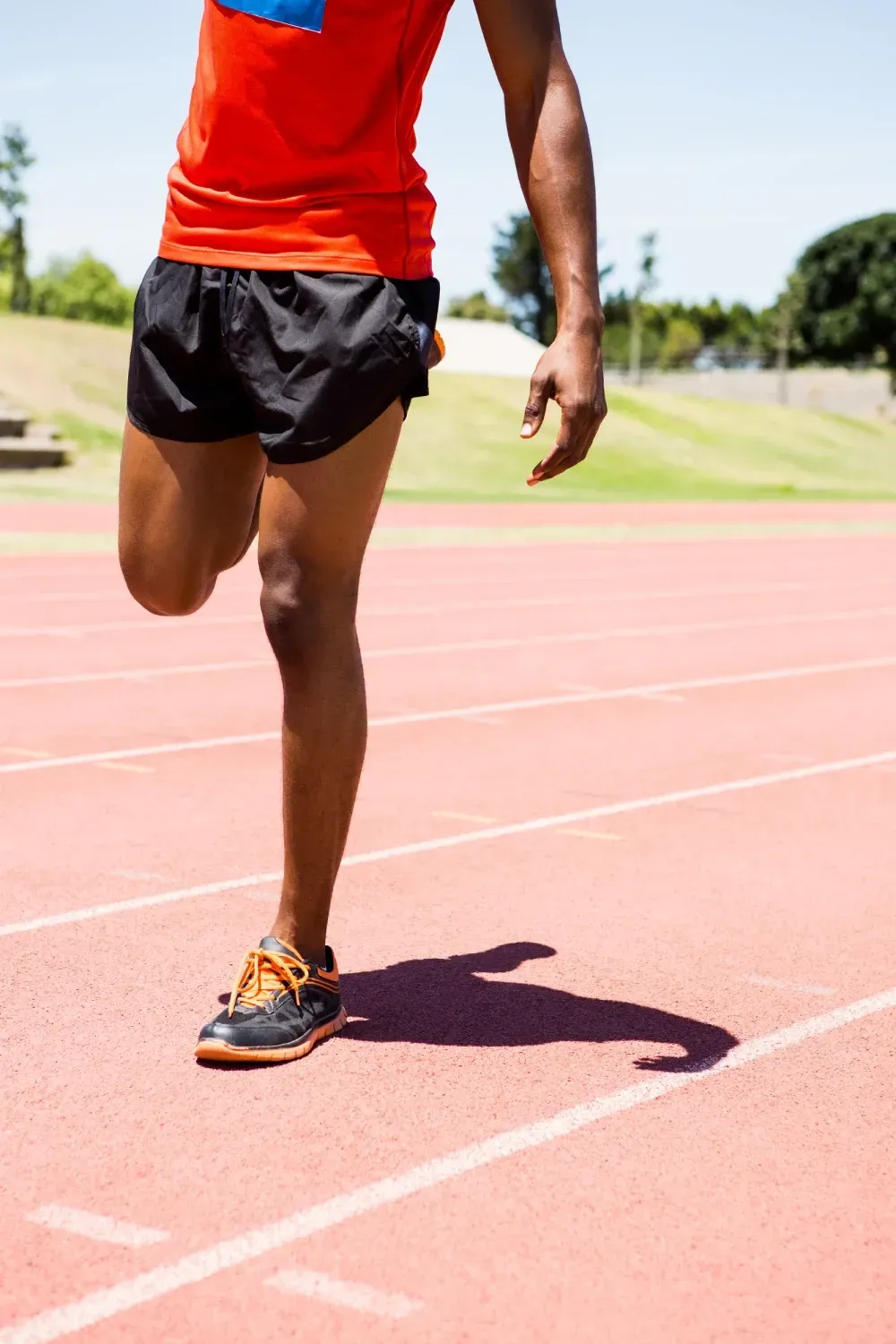 Un hombre con una camiseta naranja y pantalones cortos negros está corriendo en una pista.