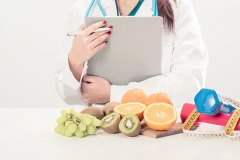 Una doctora está sentada en una mesa con fruta y cinta métrica.