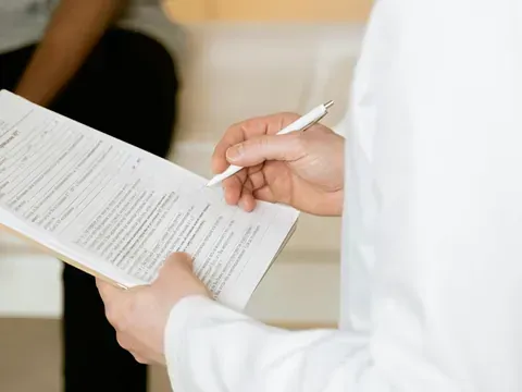 Un médico sostiene un portapapeles y escribe en él mientras un paciente está sentado en un sofá.